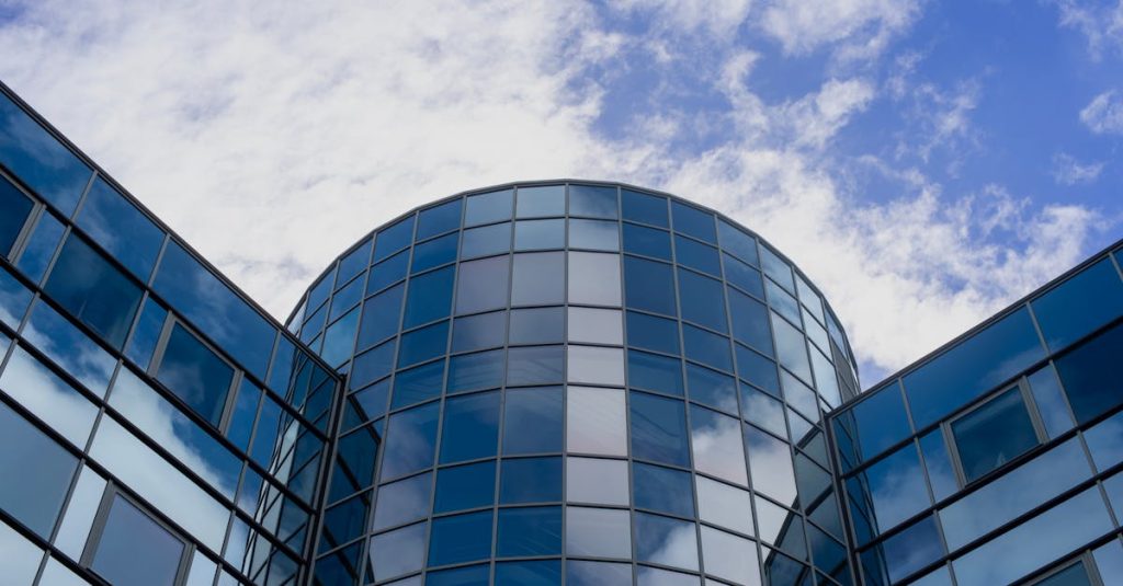 Contemporary glass building facade reflecting blue sky and clouds, showcasing modern architecture.